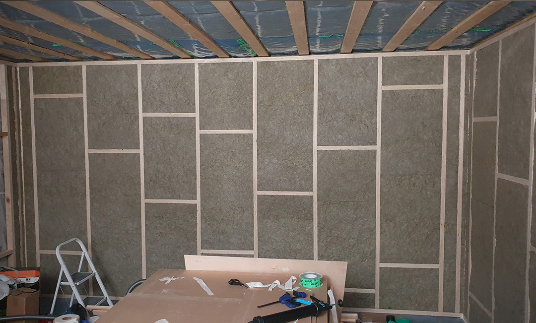 Room-within-a-room framing stage showing the inner wall structure inside the garage with rock wool